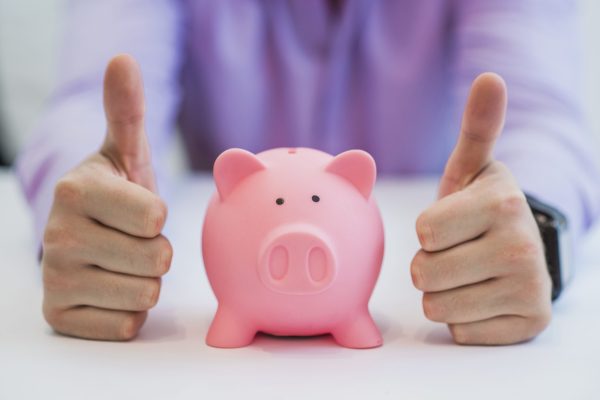 Successful business man with piggy bank holding thumbs up in office